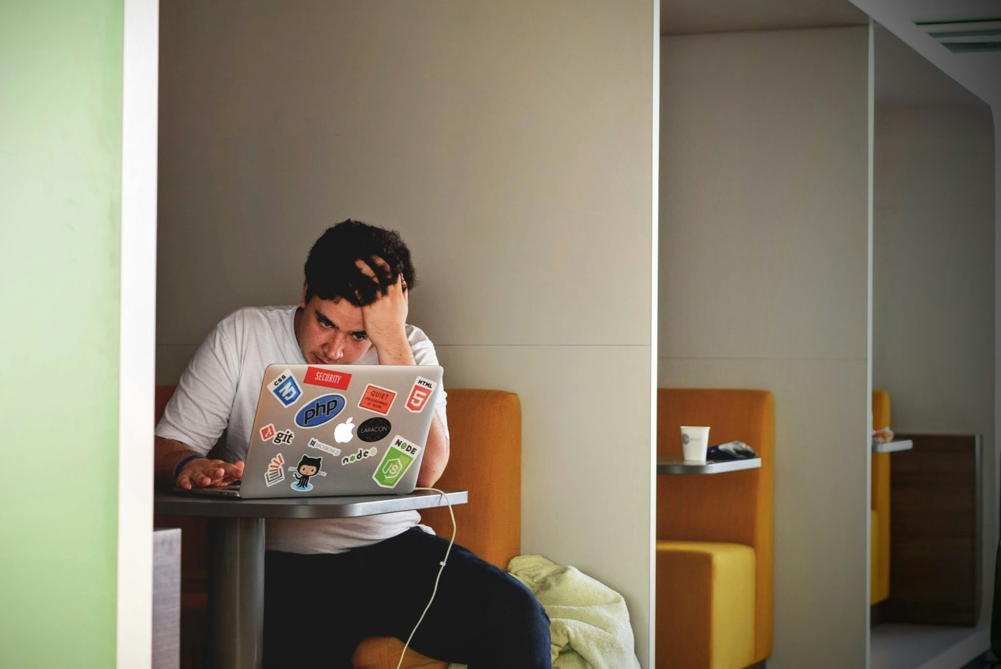 A frustrated student working on a laptop in a quiet booth.