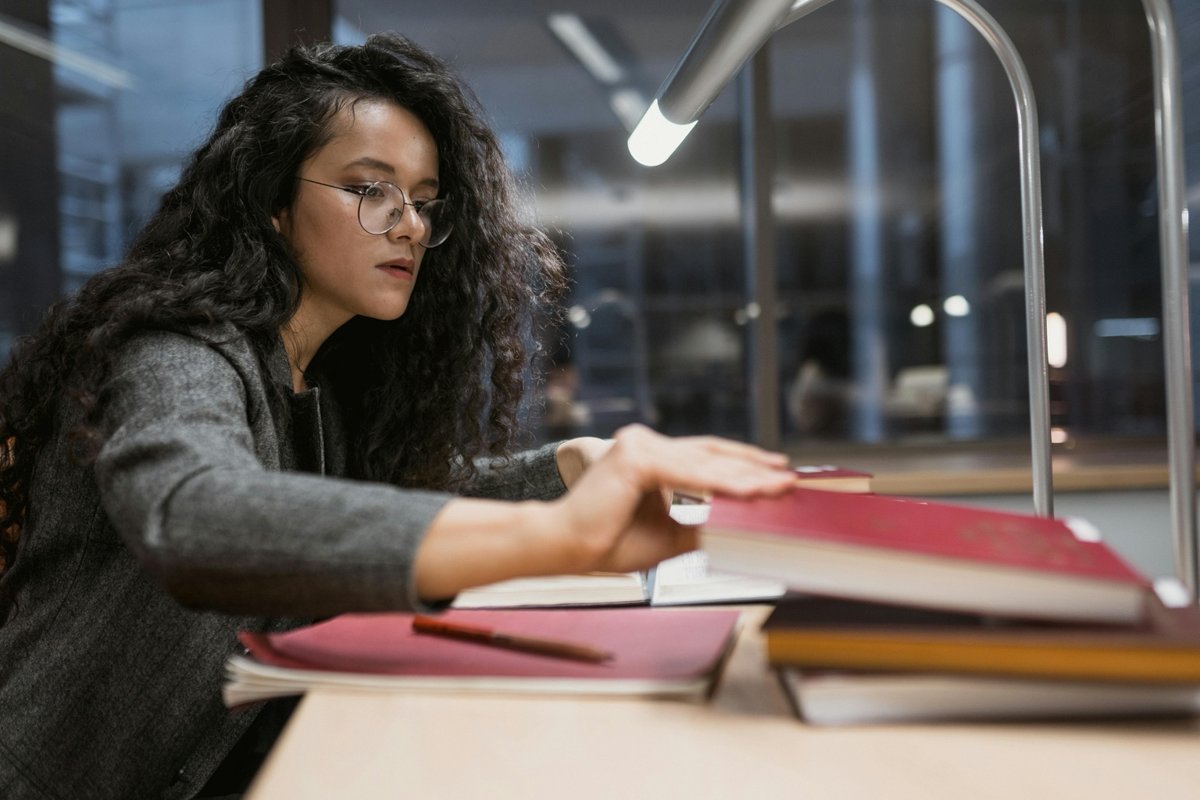 A female student with black curly hair reaches for a book in a study zone.