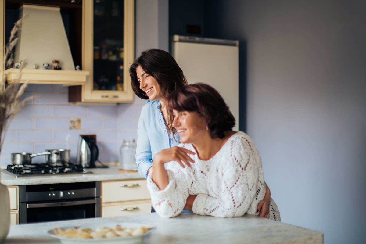 A mum and daughter laugh in the kitchen.