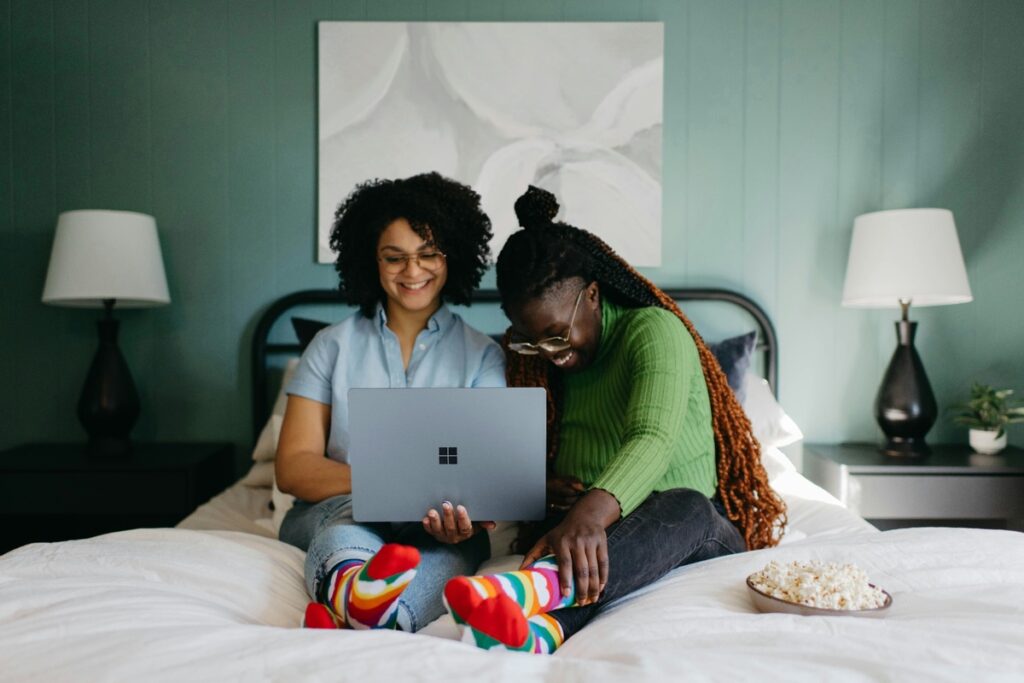 Two young Black women research student loans on a shared laptop with snacks.