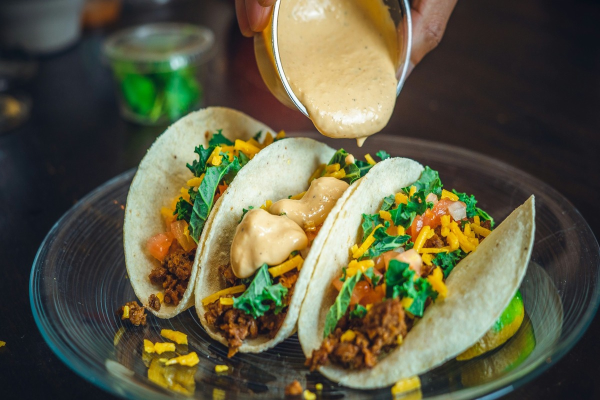 A customer pours sauce over three tasty Mexican tacos.